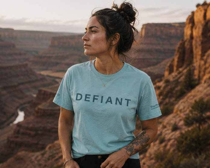Defiant Women's Relaxed T-Shirt at an Eastern Washington canyon — queer-owned PNW Pride apparel, front view
