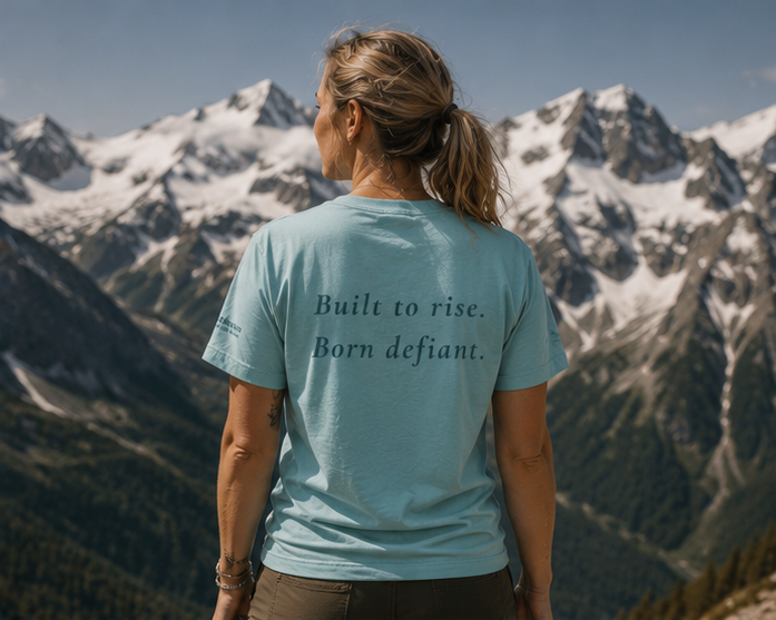 Defiant Women's Relaxed T-Shirt at a snowy Pacific Northwest mountain — queer-owned PNW Pride apparel, back view with inspirational quote