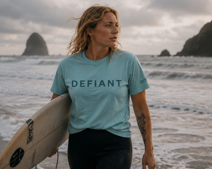 Defiant Women's Relaxed T-Shirt on a stormy Pacific Northwest coast surf — queer-owned PNW Pride apparel, front view