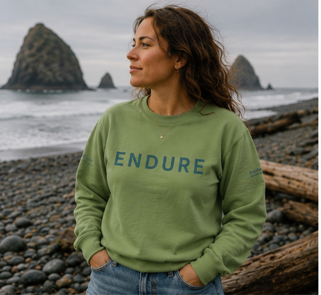 Endure Sweatshirt on the rocky Pacific Northwest coast — queer-owned PNW Pride apparel, front view