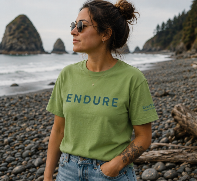 Endure T-Shirt on the rocky Pacific Northwest coast — queer-owned PNW Pride apparel, front view