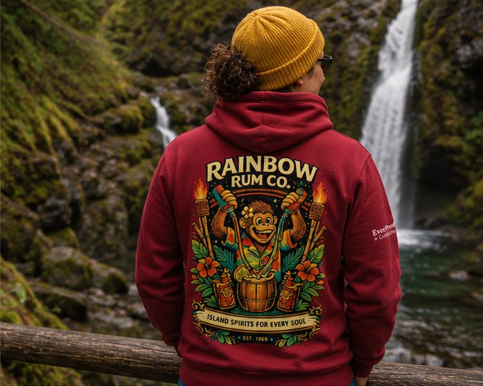 Rainbow Rum Hoodie at a Pacific Northwest forest waterfall — queer-owned PNW Pride apparel, back view