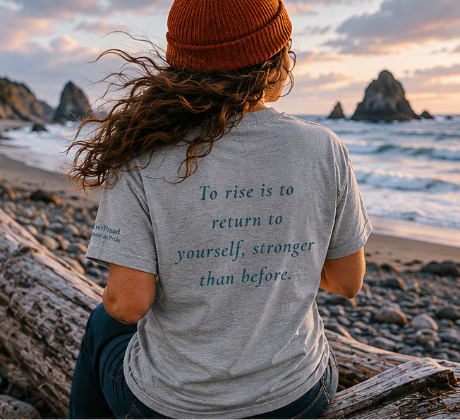 Rise T-Shirt on a driftwood-strewn Pacific coast — queer-owned PNW Pride apparel, back view