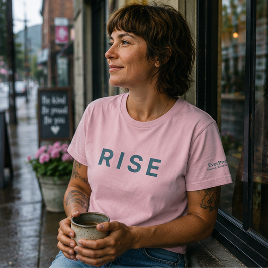 Rise Women's Relaxed T-Shirt at a rainy Pacific Northwest small-town coffee shop — queer-owned PNW Pride apparel, front view